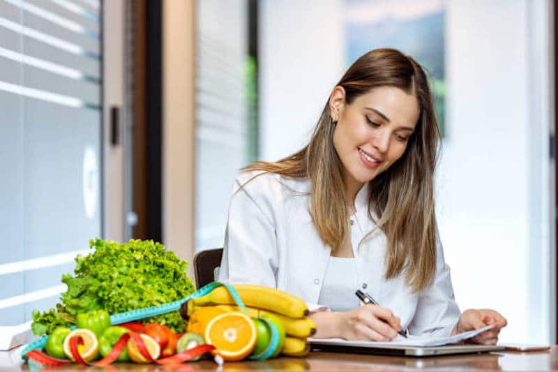 Smiling nutritionist in her office, she is showing healthy vegetables and fruits.